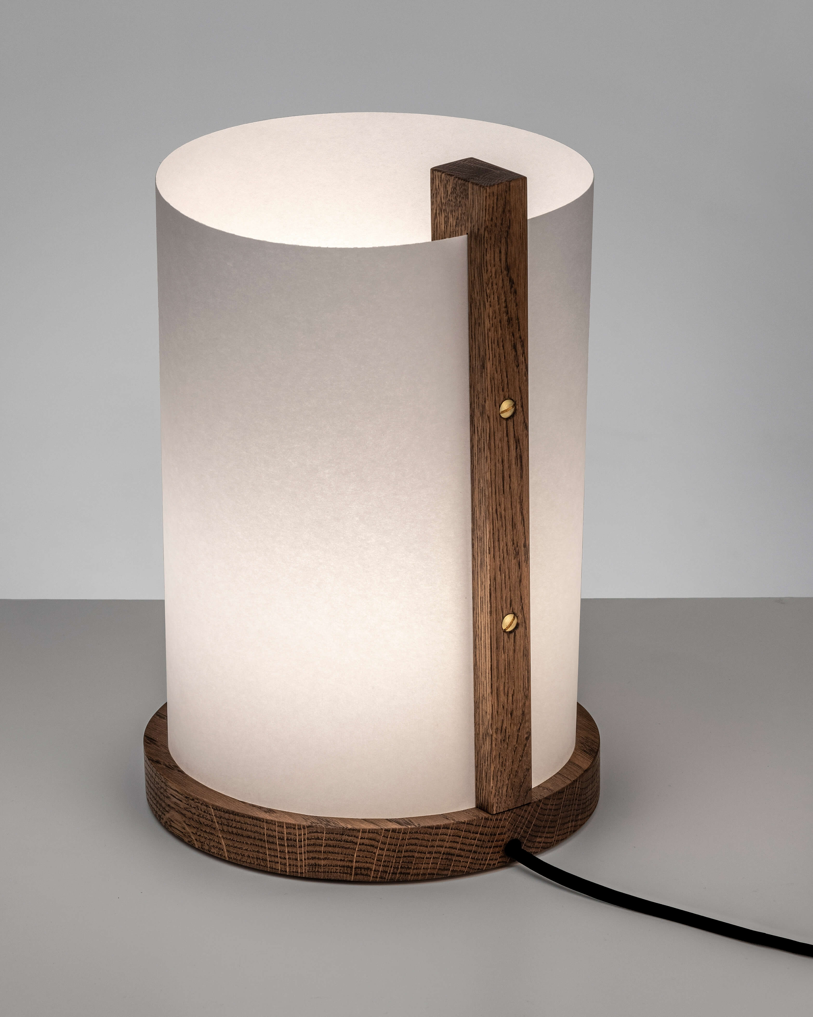Enso table lamp in washi paper and solid oak with light on, smoked finish on grey background by Motarasu