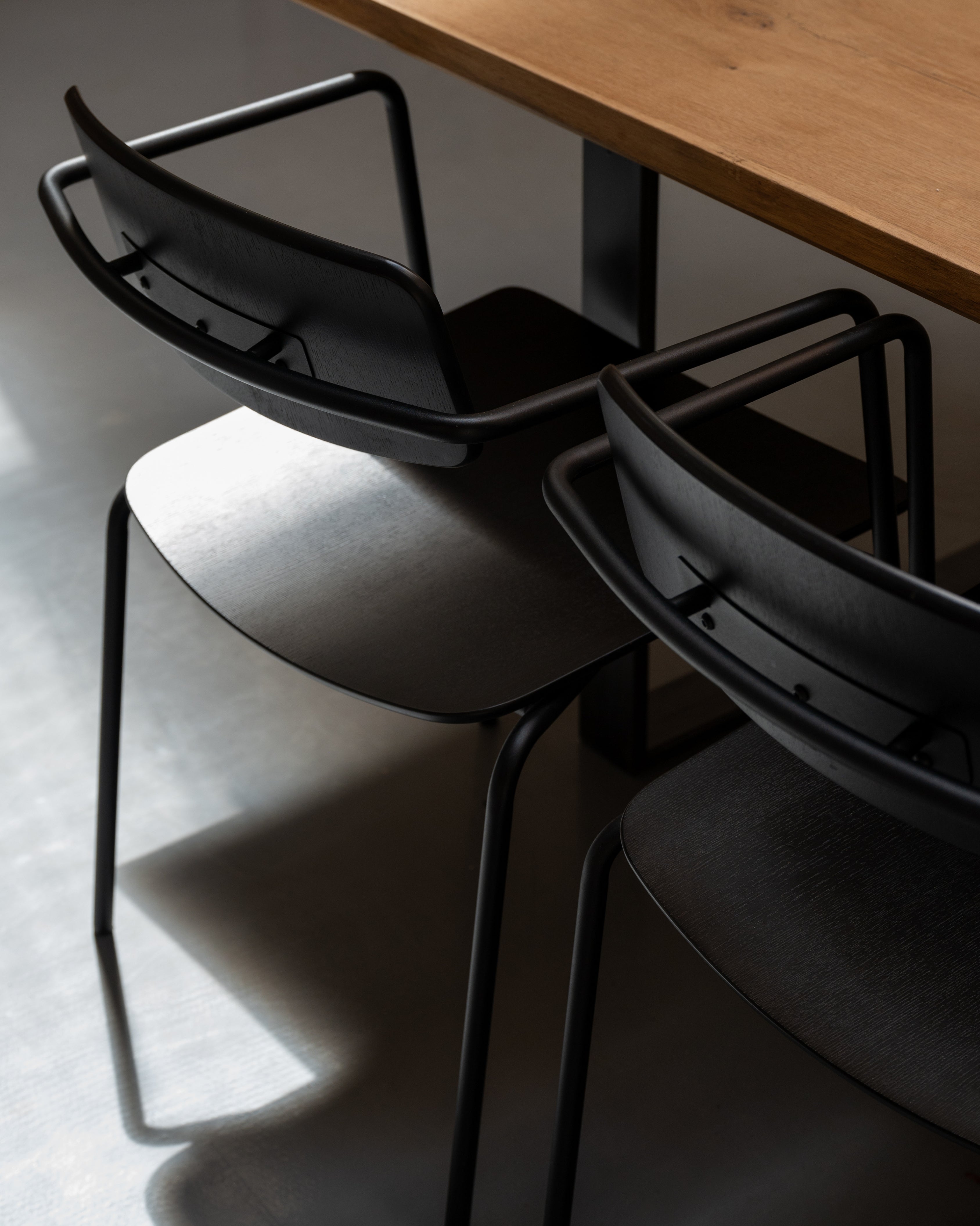 Float chair in black ash veneer, close-up of open back and steel frame detail placed next to wooden table by Motarasu
