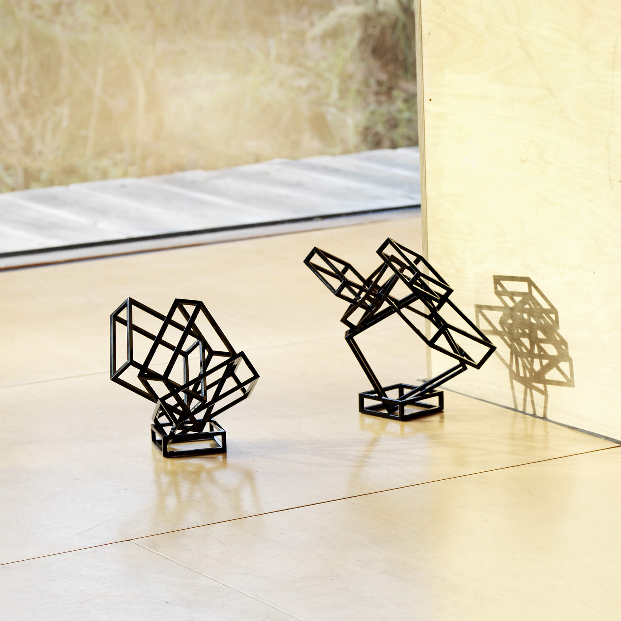 Two black coated steel sculptures placed on the floor, casting their shadows