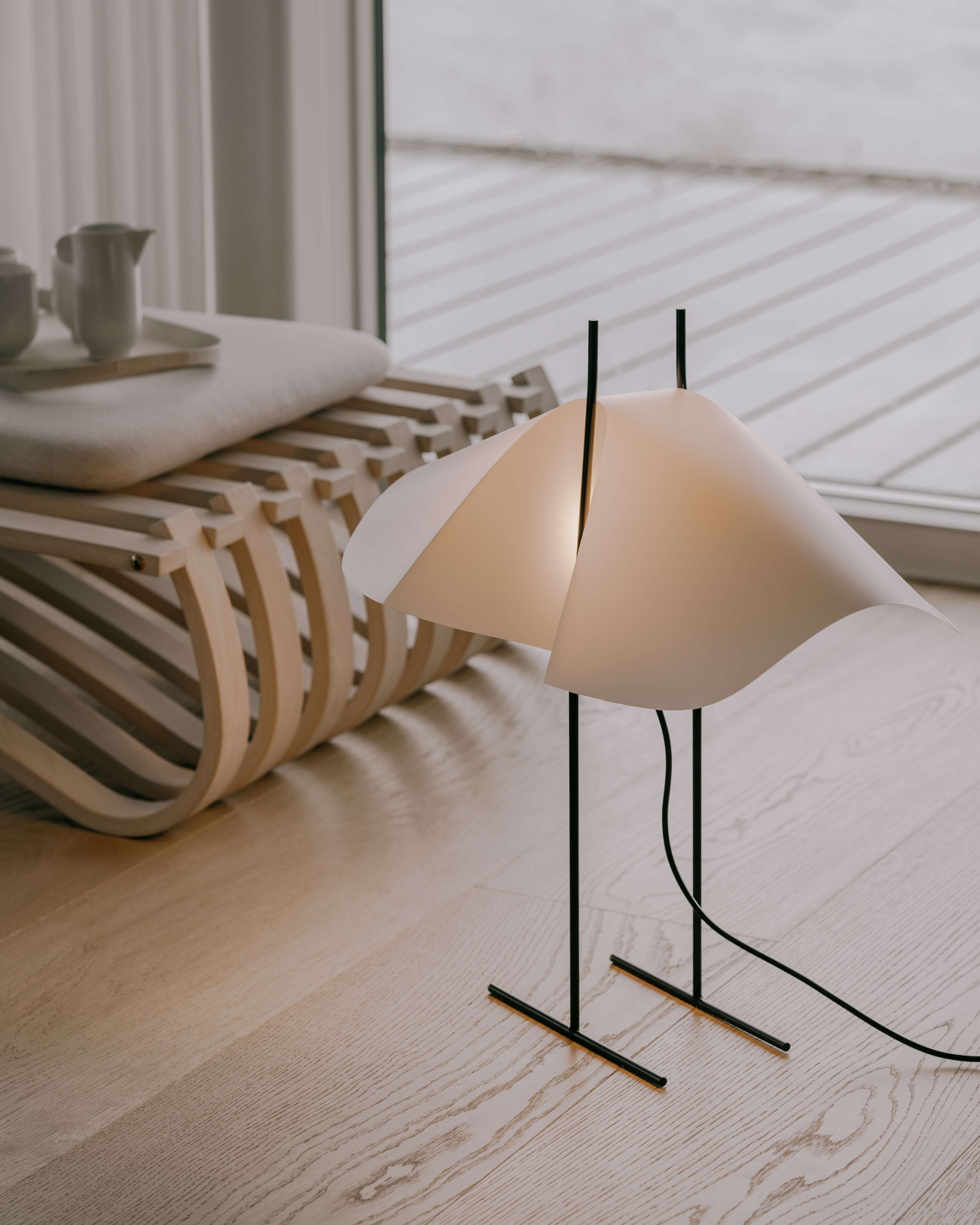 Cho floor lamp in translucent PVC with black steel base and light on, styled in a living room setting by Motarasu