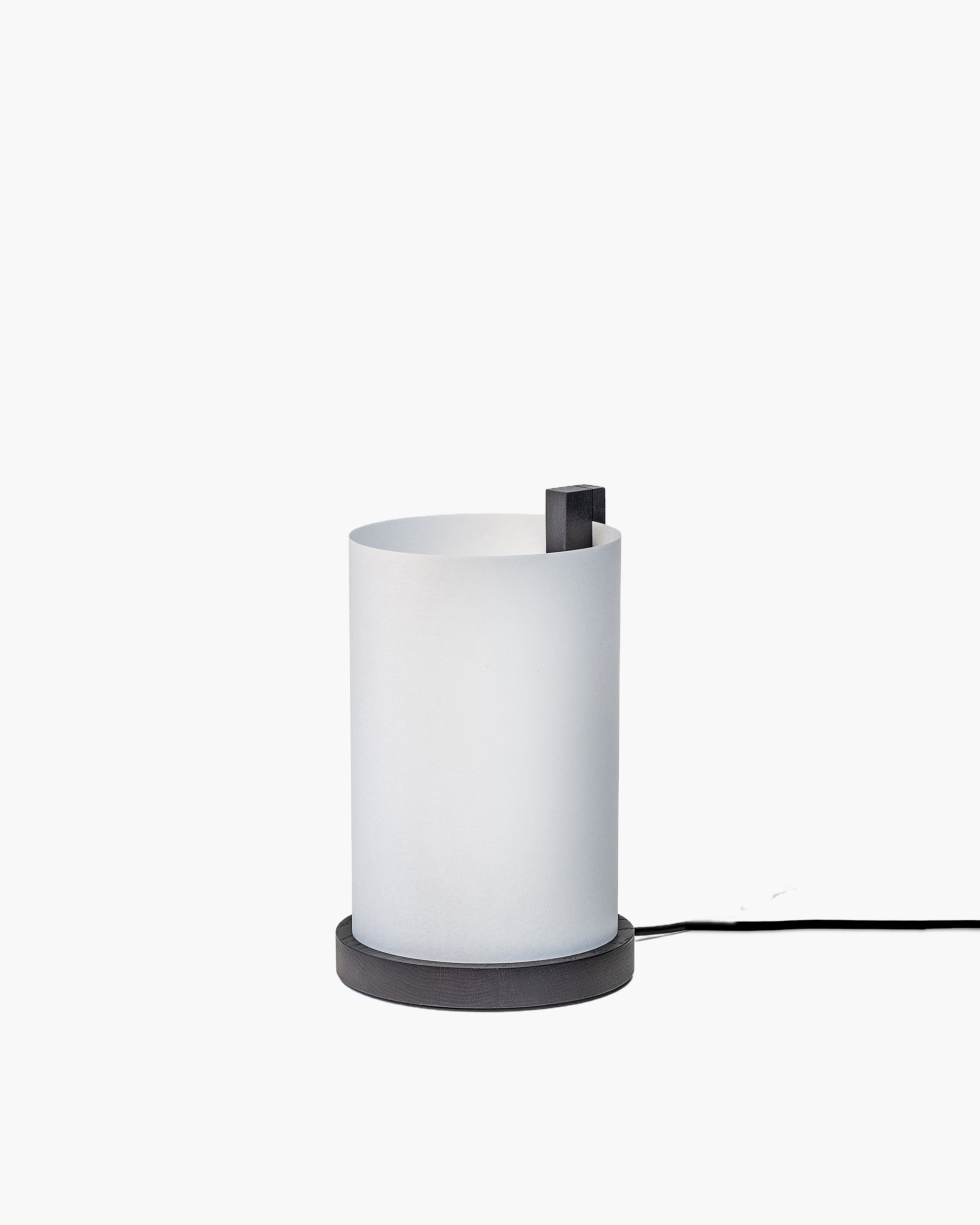 A modern table lamp with a frosted white cylindrical shade and a dark gray circular base, shown against a plain white background with its power cord extending to the right.