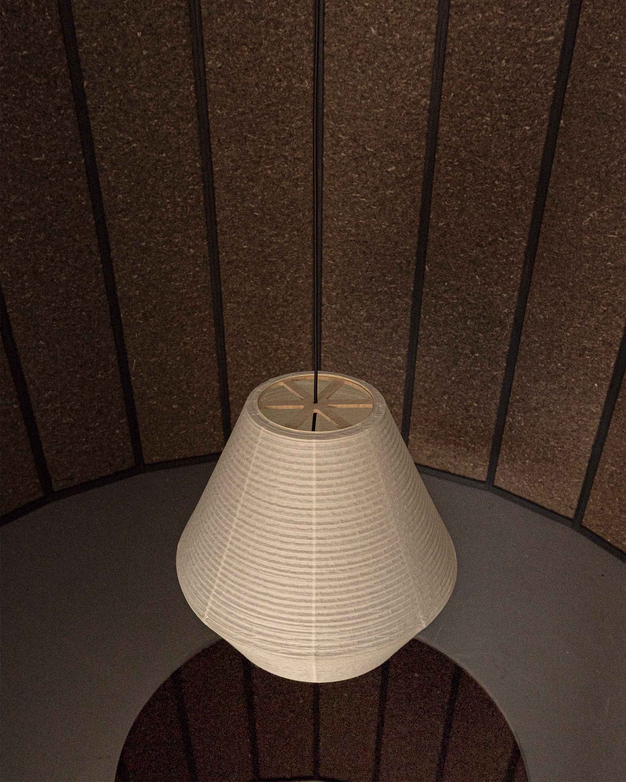 A conical paper lampshade hanging from a black cord filling the space
