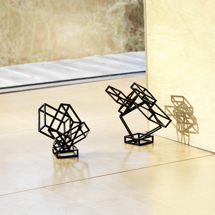 Two black coated steel  sculptures placed on the floor, casting their shadows